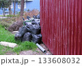 Black garbage bags near the fence of private house and an overturned trash can. 133608032