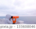 Woman in white jacket and hood looks in binoculars at sea waterfront with sea view. Side view. 133608046