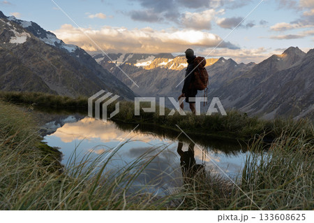 Hiker reflected in Sealy Tarns pool facing Mount Cook sunset, New Zealand 133608625