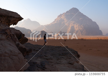 Tourist walking on rocky ledge facing Wadi Rum mountains, Jordan Tourist walking on rocky ledge facing Wadi Rum mountains, Jordan 133608735