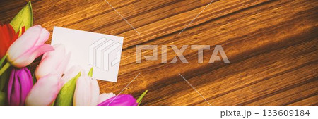 Colorful tulip bouquet and blank card are resting on flat design warm wooden tabletop, copy space 133609184