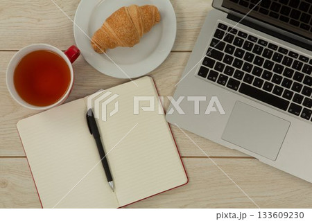 Laptop, lemon tea, croissant and diary on table 133609230