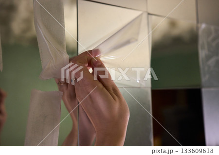 Removing protective layer to reveal clear glass, Carefully removing protective film from mirror to show pristine reflective surface in warm lit bathroom environment 133609618