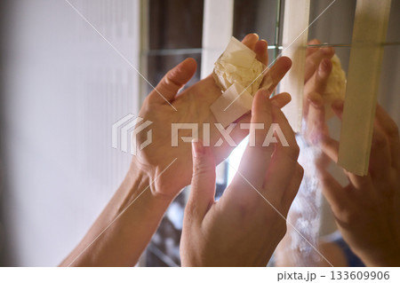 Final touch on reflective surface, Applying sponge to seal mirror tape in home renovation, Using sponge to smooth and seal mirror edge during home makeover process 133609906