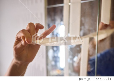 Mirror masking preparation, Detail oriented process of taping mirror for painting, Meticulous handwork involves aligning masking tape precisely on reflective glass surface 133609914