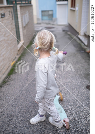 Little 4 Year Old Girl Walking Through Narrow Streets with a Scooter Without a Helmet Little 4 Year Old Girl Walking Through Narrow Streets with a Scooter Without a Helmet 133610227