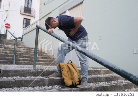 A Young Man Having a Heart Attack on the Street, Standing on the Stairs and Holding His Chest A Young Man Having a Heart Attack on the Street, Standing on the Stairs and Holding His Chest 133610252