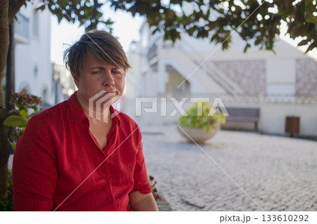 Upset overweight woman sitting alone outdoors 133610292