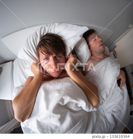 Woman covering her ears because her husband is snoring  133610364