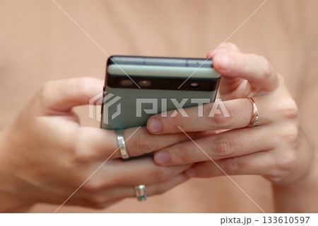 Close-up of female hands with engagement and wedding rings holding green smartphone on beige background. Close up Close-up of female hands with engagement and wedding rings holding green smartphone on beige background. Close up 133610597