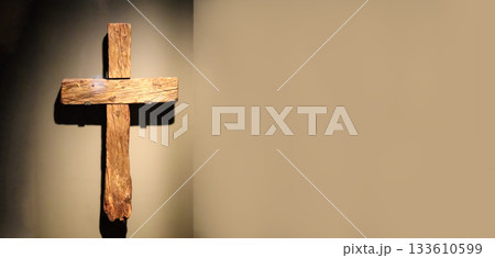 A simple, wooden cross is prominently displayed against a textured wall, symbolizing the Passion of Jesus, and is ideal for commemorating Good Friday or Holy Week. Copy space A simple, wooden cross is prominently displayed against a textured wall, symbolizing the Passion of Jesus, and is ideal for commemorating Good Friday or Holy Week. Copy space 133610599