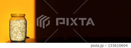 A clean banner image for healthy eating. Dry oats are prominently displayed inside a clear glass jar, set against a bright, cheerful yellow background. oats glass jar yellow banner copy space A clean banner image for healthy eating. Dry oats are prominently displayed inside a clear glass jar, set against a bright, cheerful yellow background. oats glass jar yellow banner copy space 133610604