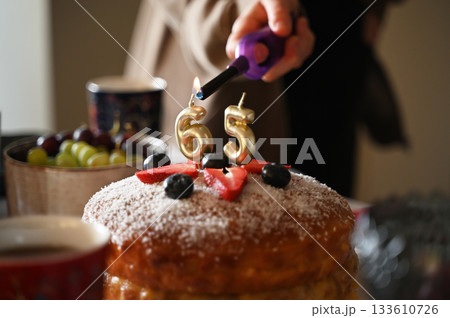 A festive close-up image capturing the moment candles are being lit on a birthday cake celebrating a 65th birthday 133610726