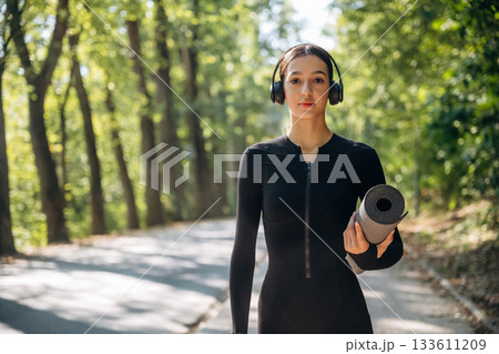 Model is with yoga mat. Young sportive skinny woman is in black fitness clothes outdoors 133611209