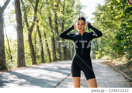Blue jumping rope, standing with it. Young sportive skinny woman is in black fitness clothes outdoors Blue jumping rope, standing with it. Young sportive skinny woman is in black fitness clothes outdoors 133611222