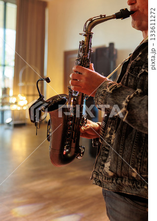 Unrecognisable professional musician plays saxophone with microphone on it for better sound at party at restaurant. Saxophonist hands using wind musical instrument at classical or jazz music concert 133611272