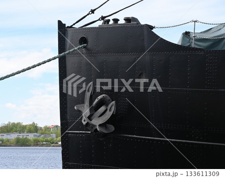 the imposing bow of a large black ship moored at a harbor, featuring a prominent steel anchor attached to its riveted metal hul 133611309