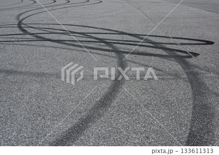 an asphalt surface covered in overlapping tire skid marks from high-speed driving maneuvers such as drifting or burnouts 133611313