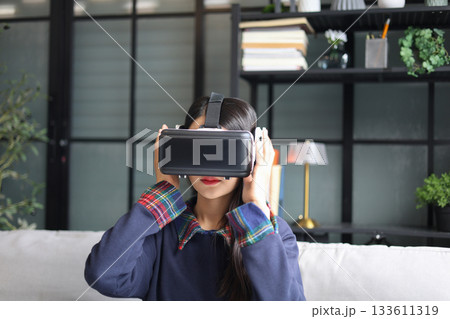 Young asian woman wearing virtual reality glasses, hand touching the air. VR headset. VR concept. Young asian woman wearing virtual reality glasses, hand touching the air. VR headset. VR concept. 133611319