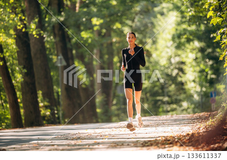 Jogging, front view. Young sportive skinny woman is in black fitness clothes outdoors Jogging, front view. Young sportive skinny woman is in black fitness clothes outdoors 133611337