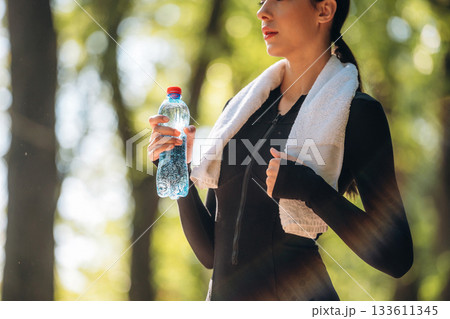With bottle of water. Young sportive skinny woman is in black fitness clothes outdoors With bottle of water. Young sportive skinny woman is in black fitness clothes outdoors 133611345