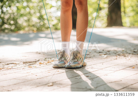 Legs of young woman that is using jumping rope. Outdoors, sunlight, close up view 133611359