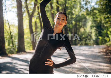 Warm up exercises. Young sportive skinny woman is in black fitness clothes outdoors 133611394