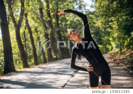 Warm up exercises. Young sportive skinny woman is in black fitness clothes outdoors 133611395