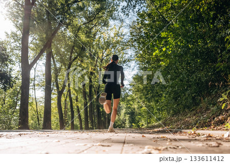 Back low view, running, jogging. Young sportive skinny woman is in black fitness clothes outdoors 133611412