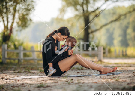 On the ground. Mother with her little son is outdoors. In sportive clothes On the ground. Mother with her little son is outdoors. In sportive clothes 133611489