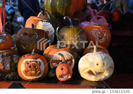 a pile of pumpkins in various shades of orange and white, with one prominently carved jack-o-lantern featuring a spooky, smiling face 133611520