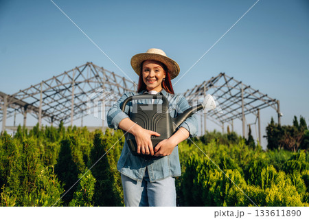 Watering can. Young redhead woman is taking care of garden 133611890