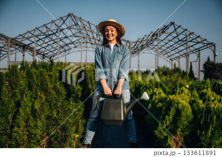 Watering can. Young redhead woman is taking care of garden 133611891