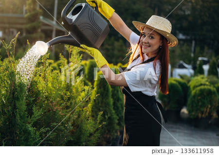 Black watering can made of plastic. Young redhead woman is taking care of garden 133611958