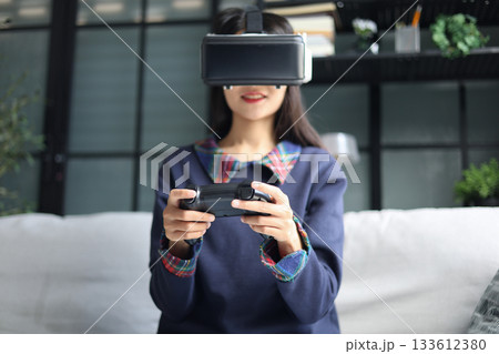 Woman play games wearing virtual reality glasses in the living room. 133612380