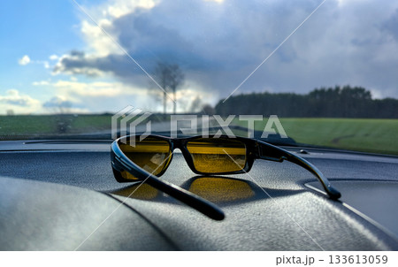 Sunglasses on the dashboard in the car. The use of the driver and protective glasses with yellow lenses for eye protection and image contrast enhancement in bright sunlight. 133613059