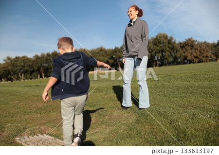 Young boy playing on grass with smiling woman 133613197