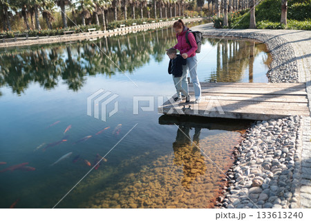 Mother and son watching koi fish in park pond Mother and son watching koi fish in park pond 133613240