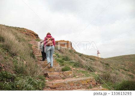 People hiking stone steps towards coastal lighthouse People hiking stone steps towards coastal lighthouse 133613293