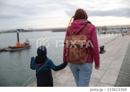 Mother and child walking hand in hand along harbor Mother and child walking hand in hand along harbor 133613300