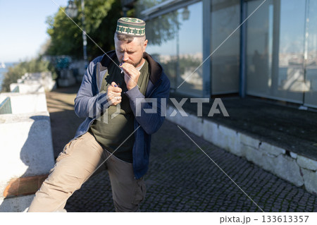 Man in kufi lighting cigarette outdoors during day Man in kufi lighting cigarette outdoors during day 133613357