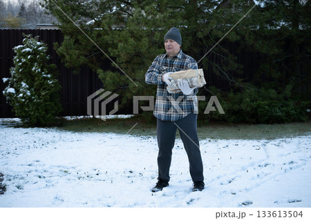 Man with firewood at snowy backyard. Winter firewood routine preparing and lighting wood stove. Energy crisis and season concept. Man with firewood at snowy backyard. Winter firewood routine preparing and lighting wood stove. Energy crisis and season concept. 133613504