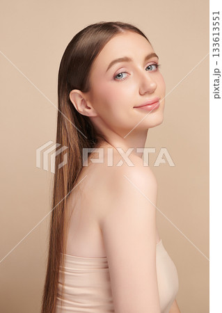 A beautiful young woman with clean, fresh skin against a beige background. Skincare, facial treatment, cosmetology, beauty, and spa. An elegant portrait of an woman. 133613551