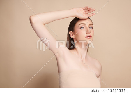 Beautiful Young woman Raises her hands to Showcase clean and hygienic underarms Against a beige background, Smooth armpit cleanliness and protection concept 133613554