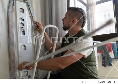 Man repairing ironing board with screwdriver at home 133613614