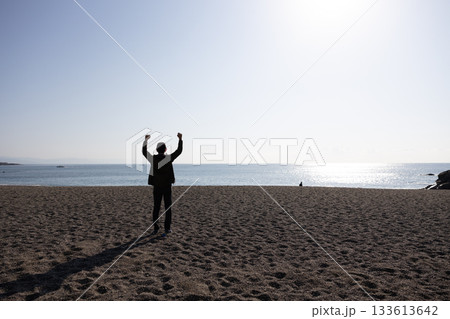 海に向かって両手を上げている一人の男性の後ろ姿 海に向かって両手を上げている一人の男性の後ろ姿 133613642