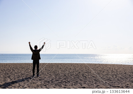 海に向かって両手を上げている一人の男性の後ろ姿 133613644