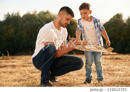 The problem, fixing it. Father and son are with wooden toy plane on the field The problem, fixing it. Father and son are with wooden toy plane on the field 133613783