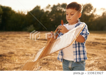 Fixing the toy. Boy is playing with wooden plane outdoors on the field 133613927