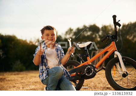 Holding wrench. Cute boy is with his bicycle on the field 133613932